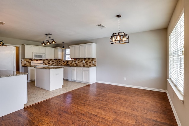 kitchen with a center island, light wood finished floors, visible vents, decorative backsplash, and white appliances