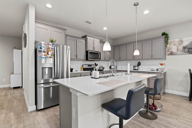 kitchen with decorative light fixtures, stainless steel appliances, light wood-type flooring, a kitchen island with sink, and a kitchen breakfast bar