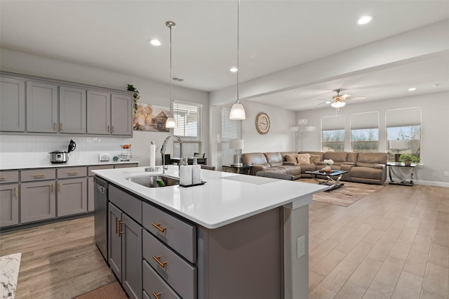 kitchen featuring dishwasher, gray cabinets, an island with sink, ceiling fan, and sink