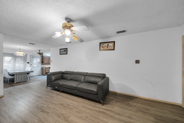 living room with a textured ceiling, ceiling fan, and wood-type flooring