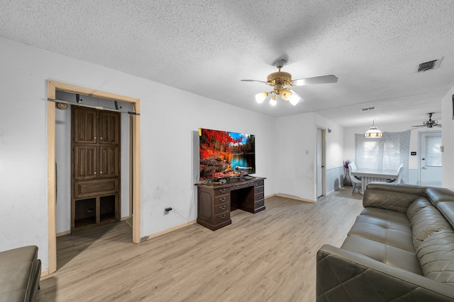 living room with light hardwood / wood-style floors, ceiling fan, and a textured ceiling