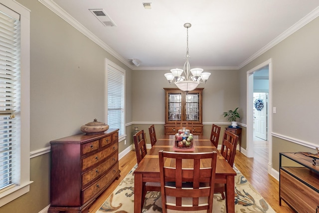 dining space with a wealth of natural light, crown molding, a chandelier, and light hardwood / wood-style flooring