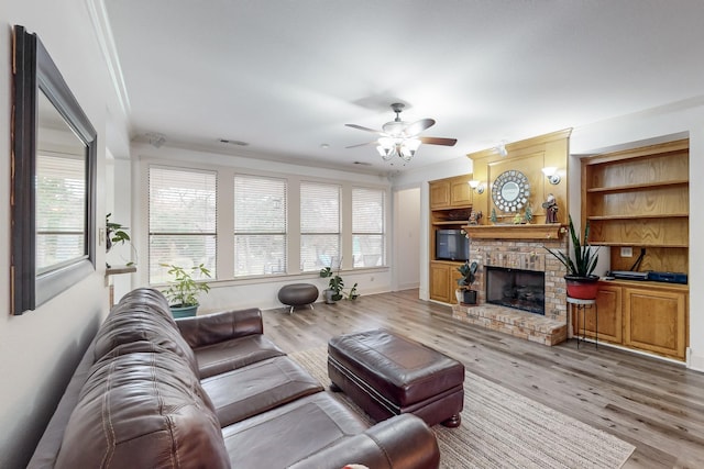 living room featuring ornamental molding, ceiling fan, light hardwood / wood-style flooring, and a brick fireplace