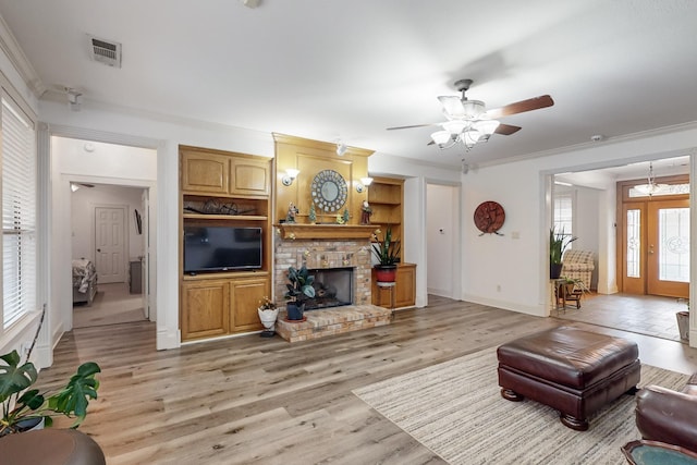 living room featuring a brick fireplace, ceiling fan, crown molding, and light wood-type flooring