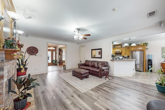 living room with ornamental molding, ceiling fan, light wood-type flooring, and a brick fireplace