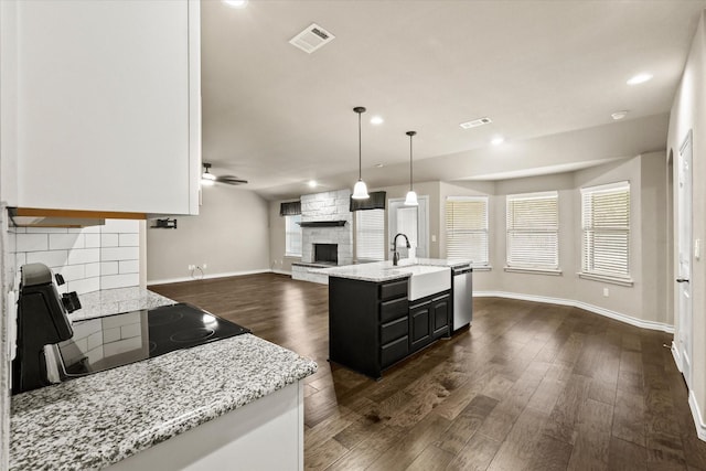 kitchen with range, a kitchen island with sink, light stone countertops, sink, and decorative light fixtures