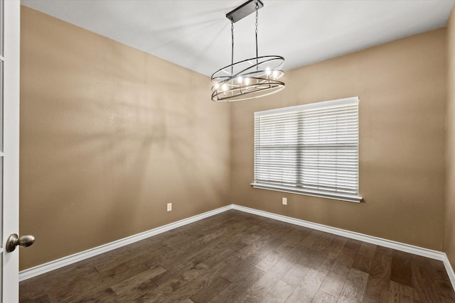 spare room featuring an inviting chandelier and dark hardwood / wood-style floors