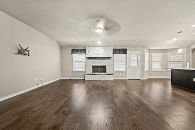 unfurnished living room with dark hardwood / wood-style floors, ceiling fan, a healthy amount of sunlight, and a stone fireplace