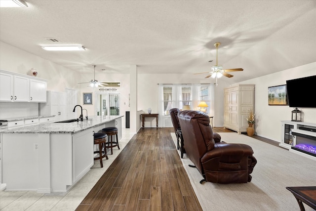 living room with vaulted ceiling, a textured ceiling, light wood-type flooring, and sink