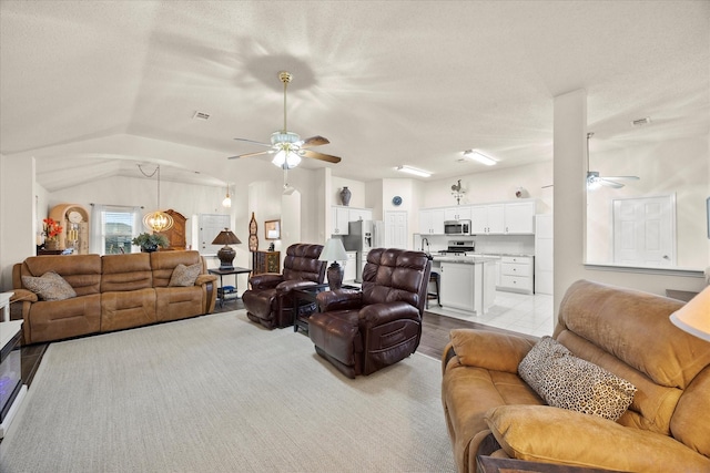 living room with vaulted ceiling, light wood-type flooring, ceiling fan, a textured ceiling, and sink