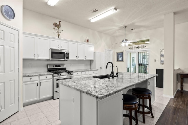 kitchen with stainless steel appliances, sink, white cabinetry, light stone counters, and a center island with sink