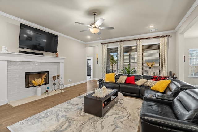 living room featuring a tiled fireplace, ornamental molding, light hardwood / wood-style floors, and a wealth of natural light