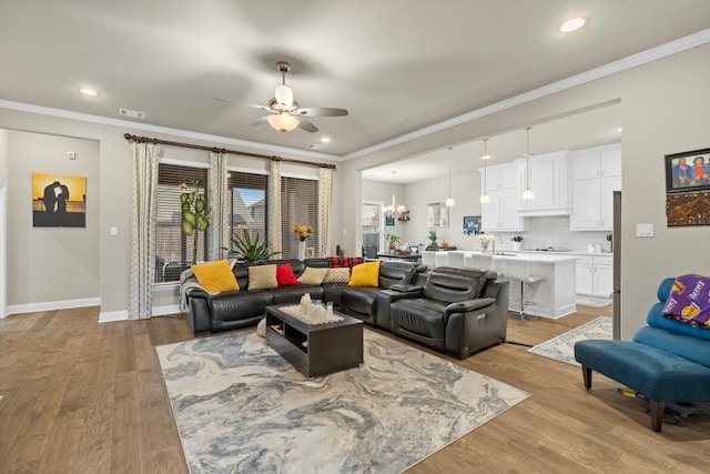 living room featuring ornamental molding, light hardwood / wood-style flooring, sink, and ceiling fan with notable chandelier