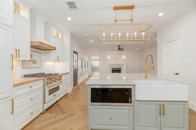 kitchen featuring sink, custom exhaust hood, white cabinetry, and high end stove