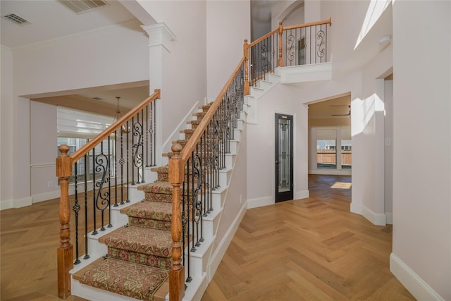 stairway with a towering ceiling, crown molding, parquet floors, and ornate columns