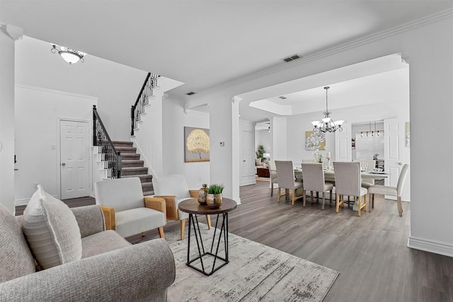 living room with a raised ceiling, wood-type flooring, crown molding, and an inviting chandelier