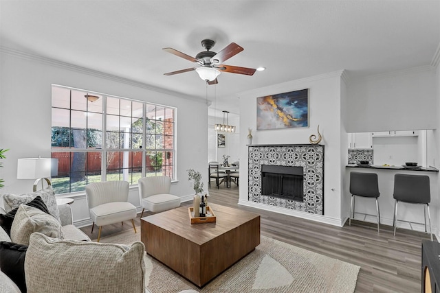 living room with ceiling fan, ornamental molding, a tile fireplace, and wood-type flooring