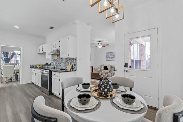 dining space featuring dark wood-type flooring, crown molding, and ceiling fan with notable chandelier