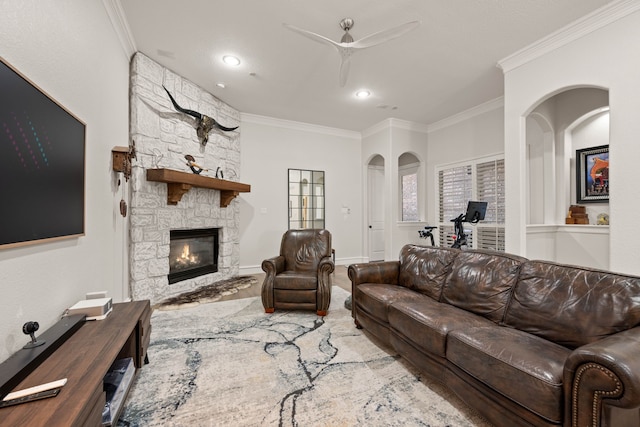 living room featuring ceiling fan, crown molding, light hardwood / wood-style flooring, and a stone fireplace