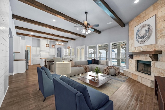 living room featuring ceiling fan, dark hardwood / wood-style flooring, beam ceiling, and a stone fireplace