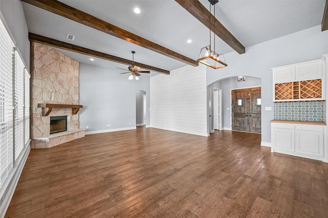 unfurnished living room with dark wood-type flooring, a fireplace, beam ceiling, and ceiling fan