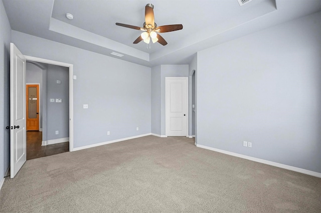 empty room featuring ceiling fan, a raised ceiling, and dark colored carpet