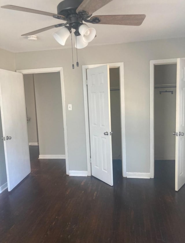 unfurnished bedroom with two closets, ceiling fan, and dark hardwood / wood-style floors