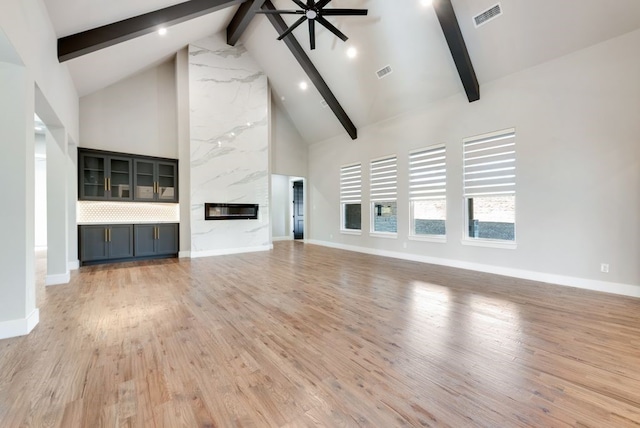 unfurnished living room featuring a high end fireplace, high vaulted ceiling, light hardwood / wood-style flooring, and beamed ceiling