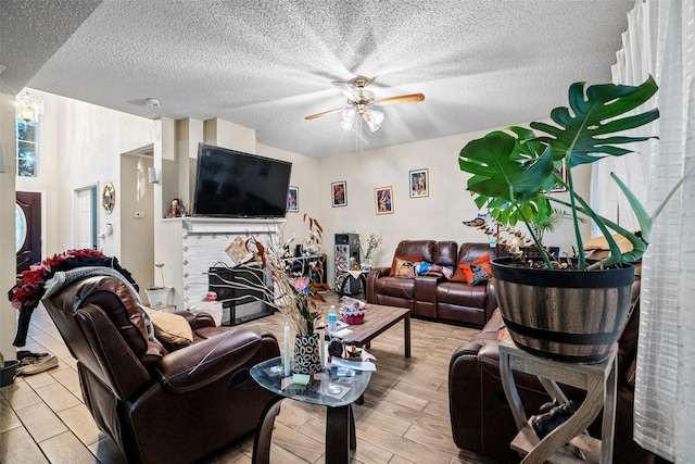 living room with a fireplace, ceiling fan, and a textured ceiling