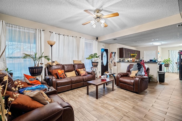 living room featuring ceiling fan, light hardwood / wood-style flooring, and a textured ceiling