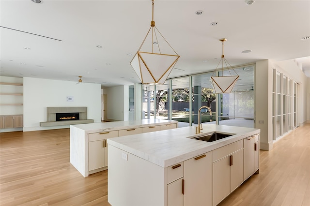 kitchen featuring a kitchen island with sink, ceiling fan, sink, light hardwood / wood-style flooring, and decorative light fixtures