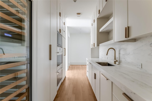 kitchen featuring light wood-type flooring, light stone counters, sink, oven, and white cabinetry