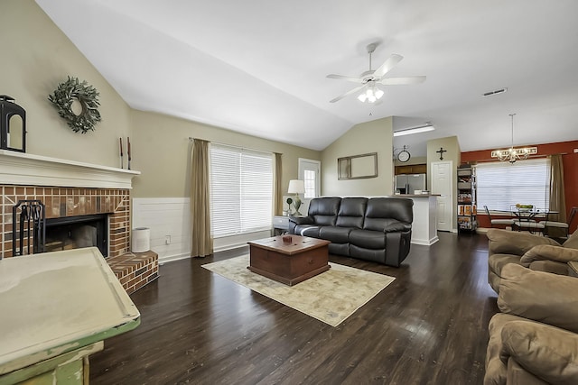 living room with dark wood-type flooring, vaulted ceiling, ceiling fan with notable chandelier, and a fireplace