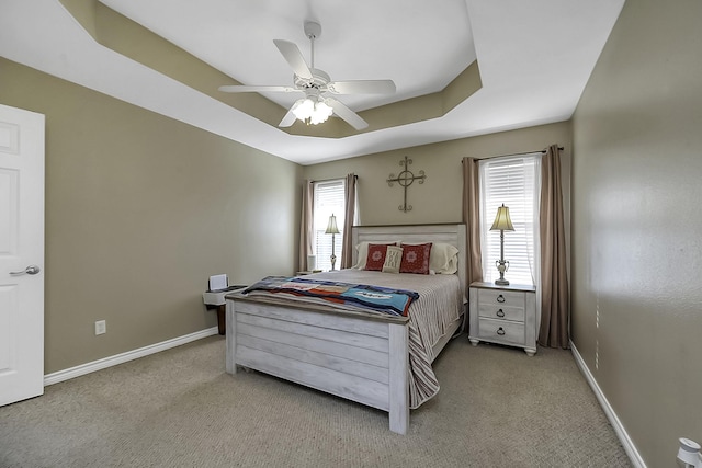 carpeted bedroom with a raised ceiling and ceiling fan