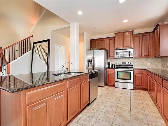 kitchen featuring stainless steel appliances, sink, decorative backsplash, dark stone counters, and a kitchen island with sink