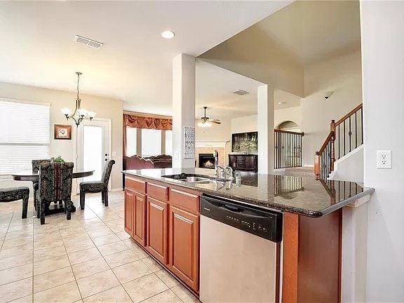 kitchen with dark stone countertops, light tile patterned floors, sink, stainless steel dishwasher, and ceiling fan with notable chandelier