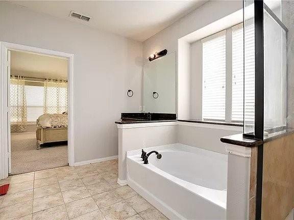 bathroom with tile patterned flooring, a tub to relax in, and a healthy amount of sunlight