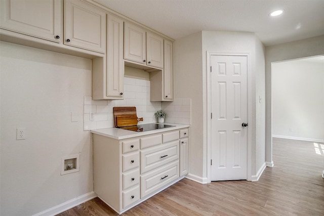 kitchen with light hardwood / wood-style flooring, cream cabinets, black electric cooktop, and backsplash