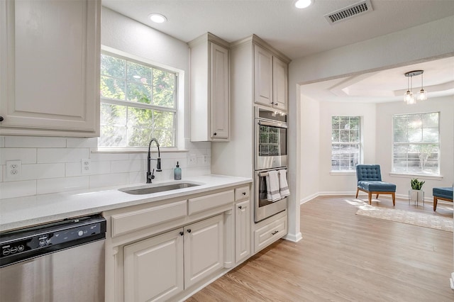 kitchen featuring sink, stainless steel appliances, decorative light fixtures, light hardwood / wood-style floors, and decorative backsplash