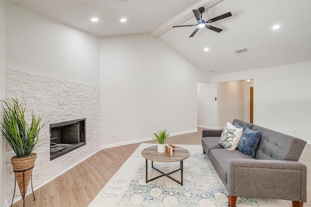 living room featuring ceiling fan, vaulted ceiling with beams, light hardwood / wood-style flooring, and a stone fireplace