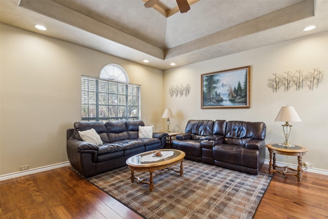 living room featuring ceiling fan, a high ceiling, wood-type flooring, and a raised ceiling