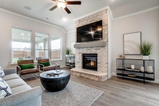 living room with vaulted ceiling, ornamental molding, hardwood / wood-style floors, a fireplace, and ceiling fan