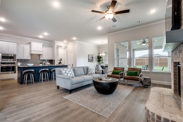 living room with ceiling fan with notable chandelier, a fireplace, ornamental molding, and light hardwood / wood-style floors