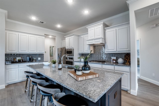 kitchen with white cabinets, stainless steel appliances, a kitchen island with sink, and light stone counters