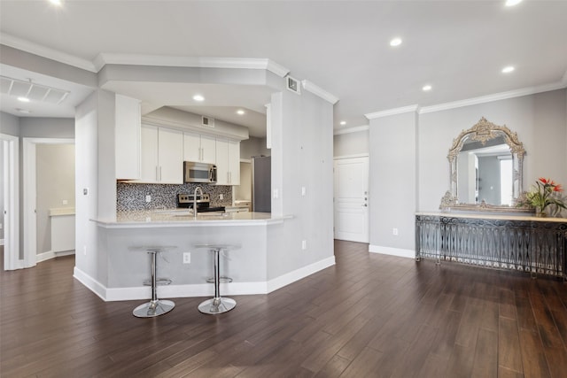 kitchen featuring a breakfast bar area, appliances with stainless steel finishes, kitchen peninsula, white cabinets, and backsplash