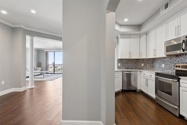 kitchen with stainless steel appliances, white cabinetry, decorative columns, and dark wood-type flooring