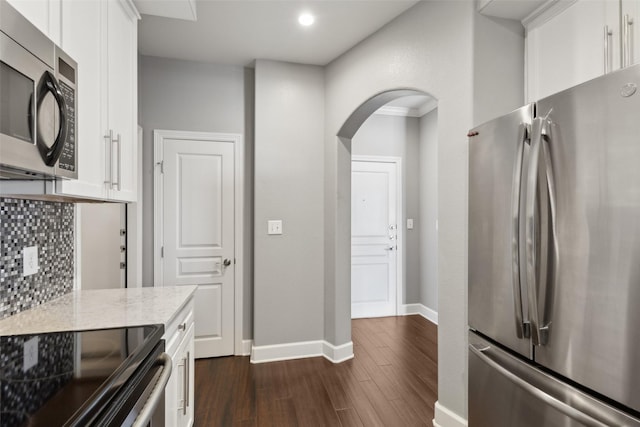 kitchen featuring stainless steel appliances, white cabinetry, light stone counters, backsplash, and dark wood-type flooring