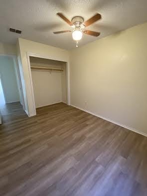 unfurnished bedroom with a closet, ceiling fan, a textured ceiling, and dark wood-type flooring