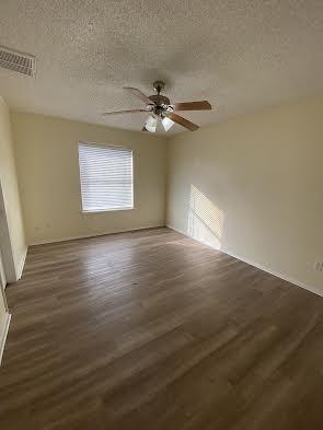 unfurnished room with visible vents, a ceiling fan, dark wood-type flooring, baseboards, and a textured ceiling