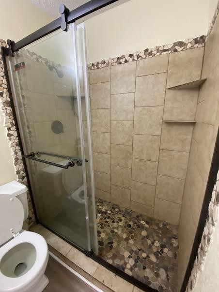 bathroom featuring a shower with door and toilet